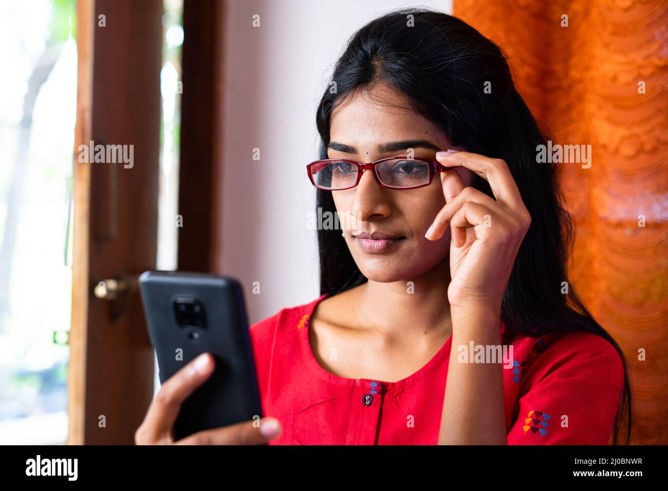 Junges Mädchen mit Brille beschäftigt mit Handy zu Hause - Konzept der sozialen Medien, Internet und Sehvermögen Problem Stockfoto