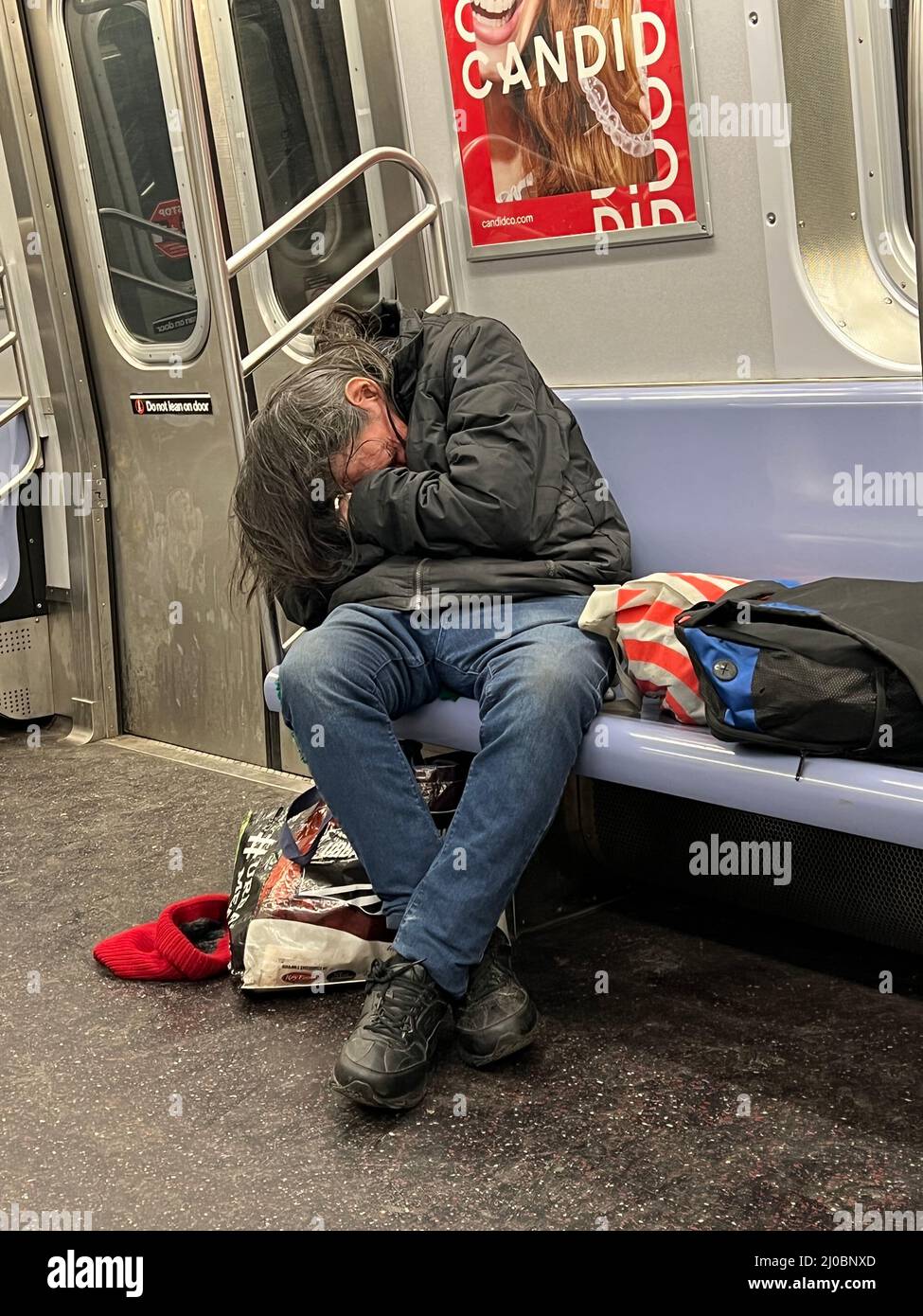 Obdachloser mit seinen Habseligkeiten schläft im Winter in Brooklyn, New York, in einem F-Zug. Stockfoto