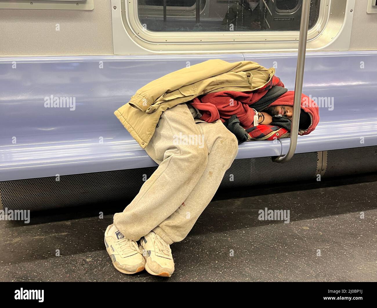 Müde junge Mann breitete sich auf einem U-Bahn-Sitz in einem Zug aus, der durch Manhattan fuhr. Stockfoto
