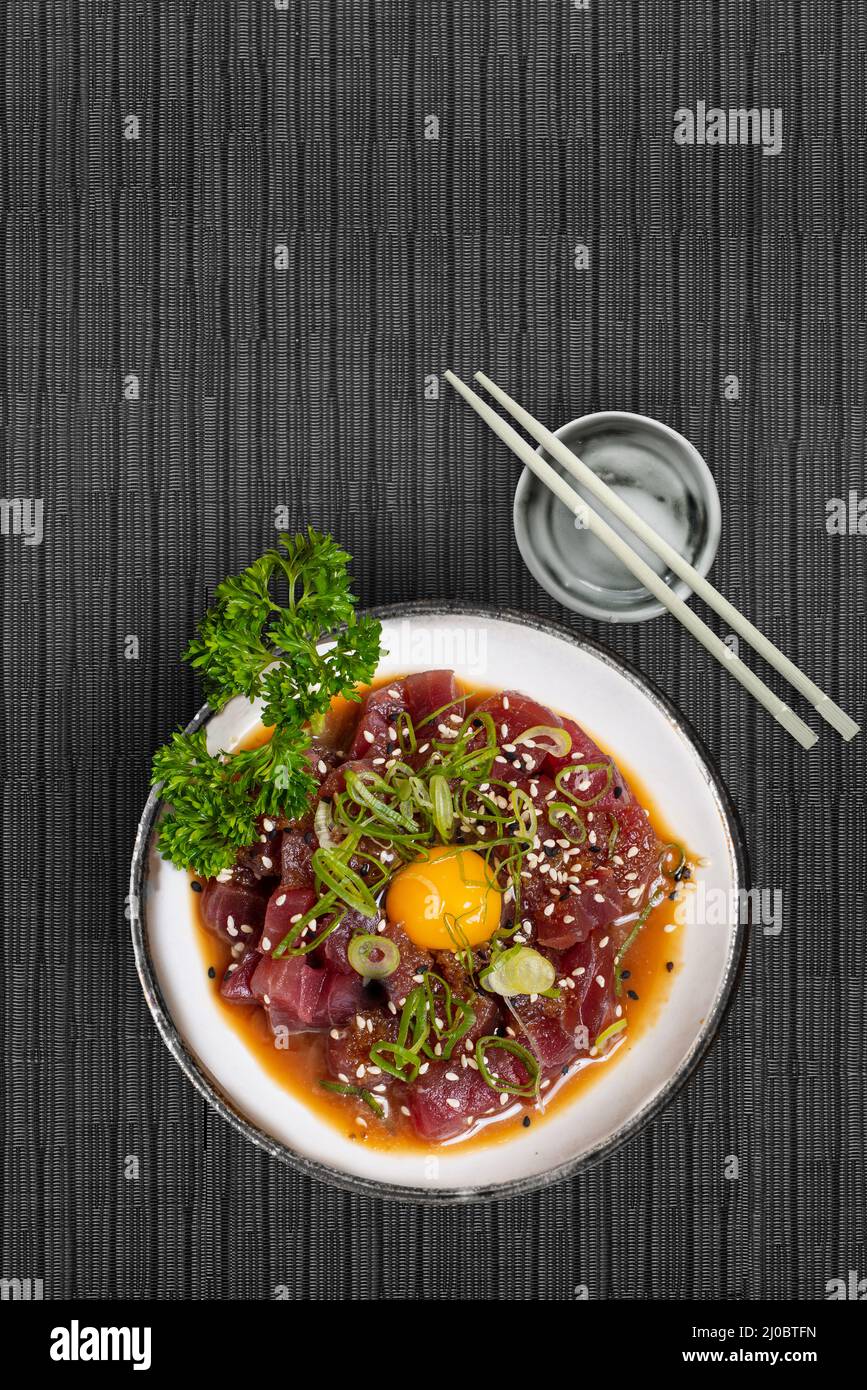 Maguro Thunfisch-Tartar mit Sesam-Schnittlauch-Algen und Wachtelei auf japanischer Tischdecke mit Essstäbchen senkrecht mit Kopierfläche oben Stockfoto