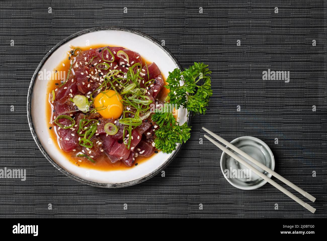 Maguro Thunfisch-Tartar mit Sesam-Schnittlauch-Algen und Wachtelei auf japanischer Tischdecke mit Essstäbchen Stockfoto