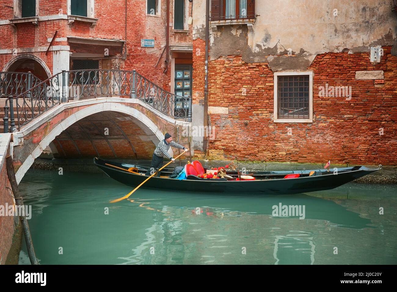 Gondoliere segelt mit seiner Gondel unter der Brücke durch den Kanal in Venedig, Italien Stockfoto