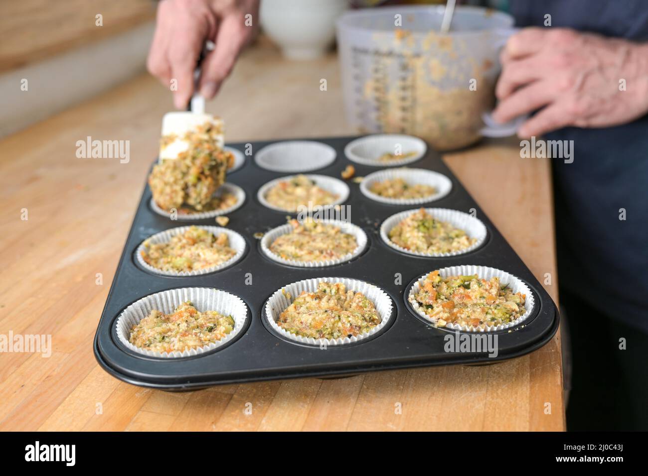 Hände eines Mannes, der Gemüseteig in ein Muffin-Backblech füllt für gesunde, herzhafte Cupcakes, vegetarische und vegane Low Carb-Diät, ausgewählter Fokus, schmal Stockfoto