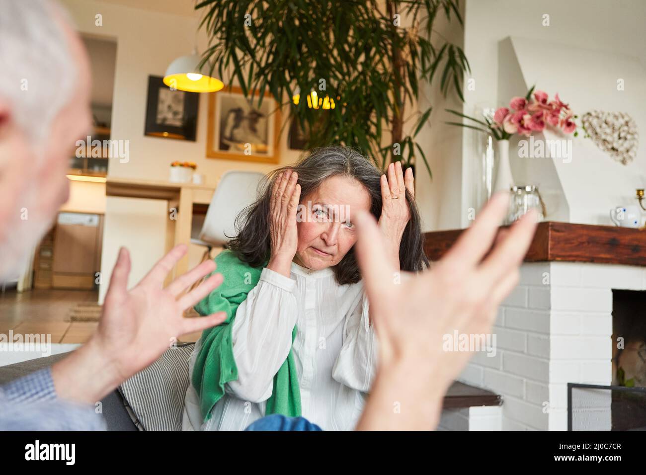 Ältere Frau, die Ohren bedeckt, während sie mit einem wütenden Mann als Konzept der häuslichen Gewalt argumentiert Stockfoto