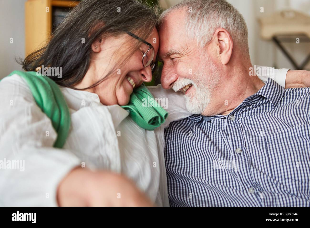 Verliebtes Senioren-Paar, das sich auf dem Sofa aus Liebe und Partnerschaft im Alter fröhlich anlächelt Stockfoto