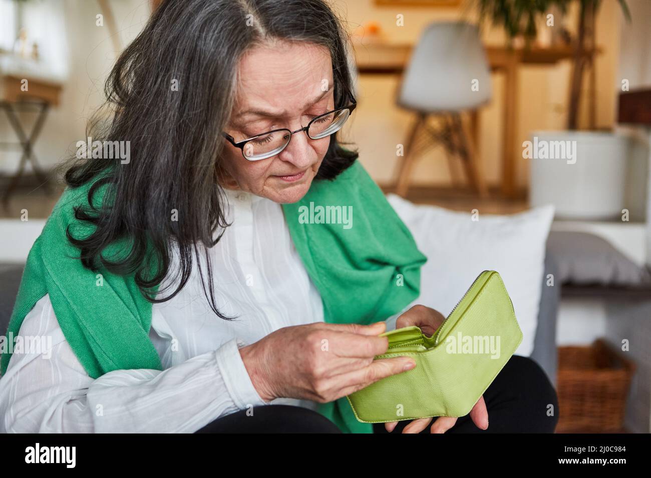 Frau als Rentnerin zu Hause, die ihre leere Brieftasche als ein Konzept der Altersarmut und Sorgen betrachtet Stockfoto