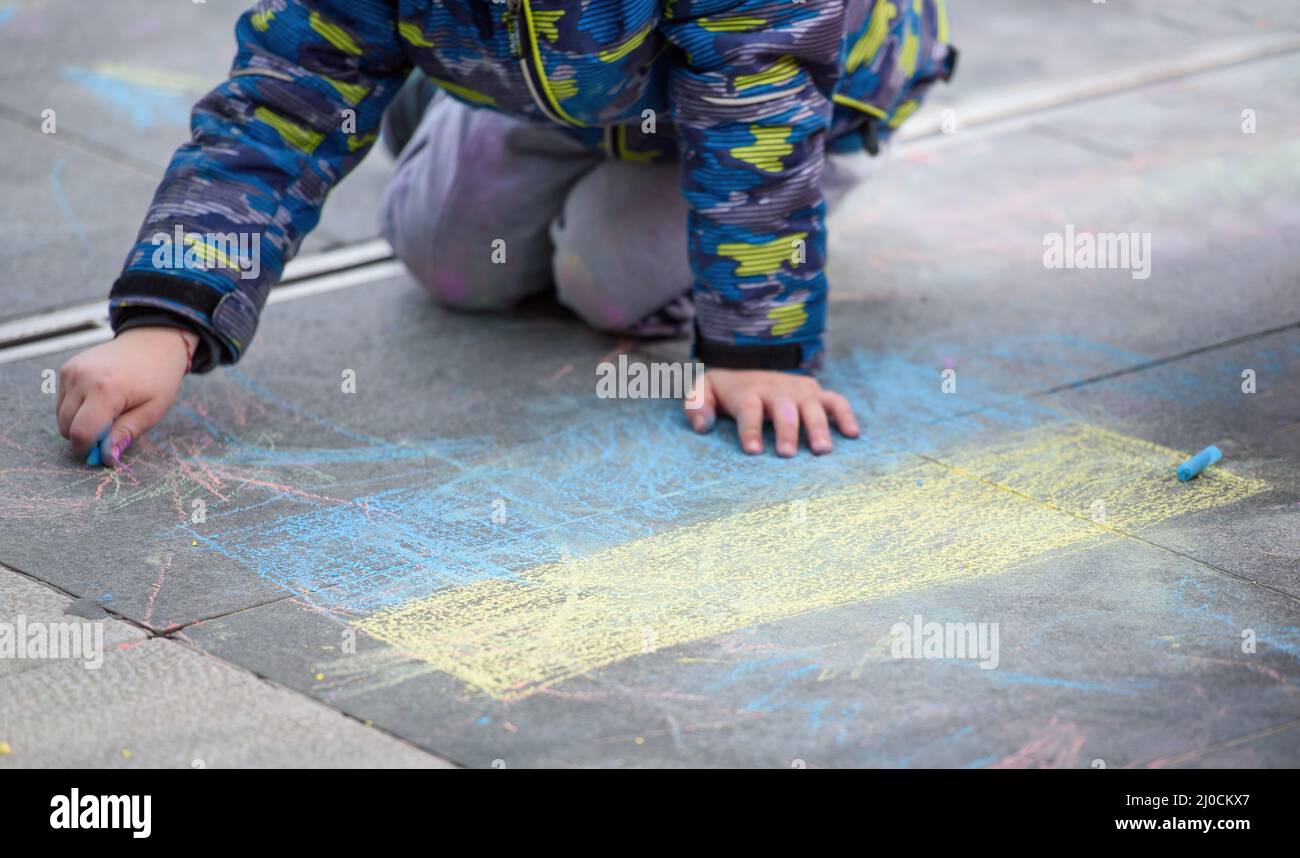 Das Kind zeichnet die blau-gelbe Flagge der Ukraine auf den Asphalt Stockfoto