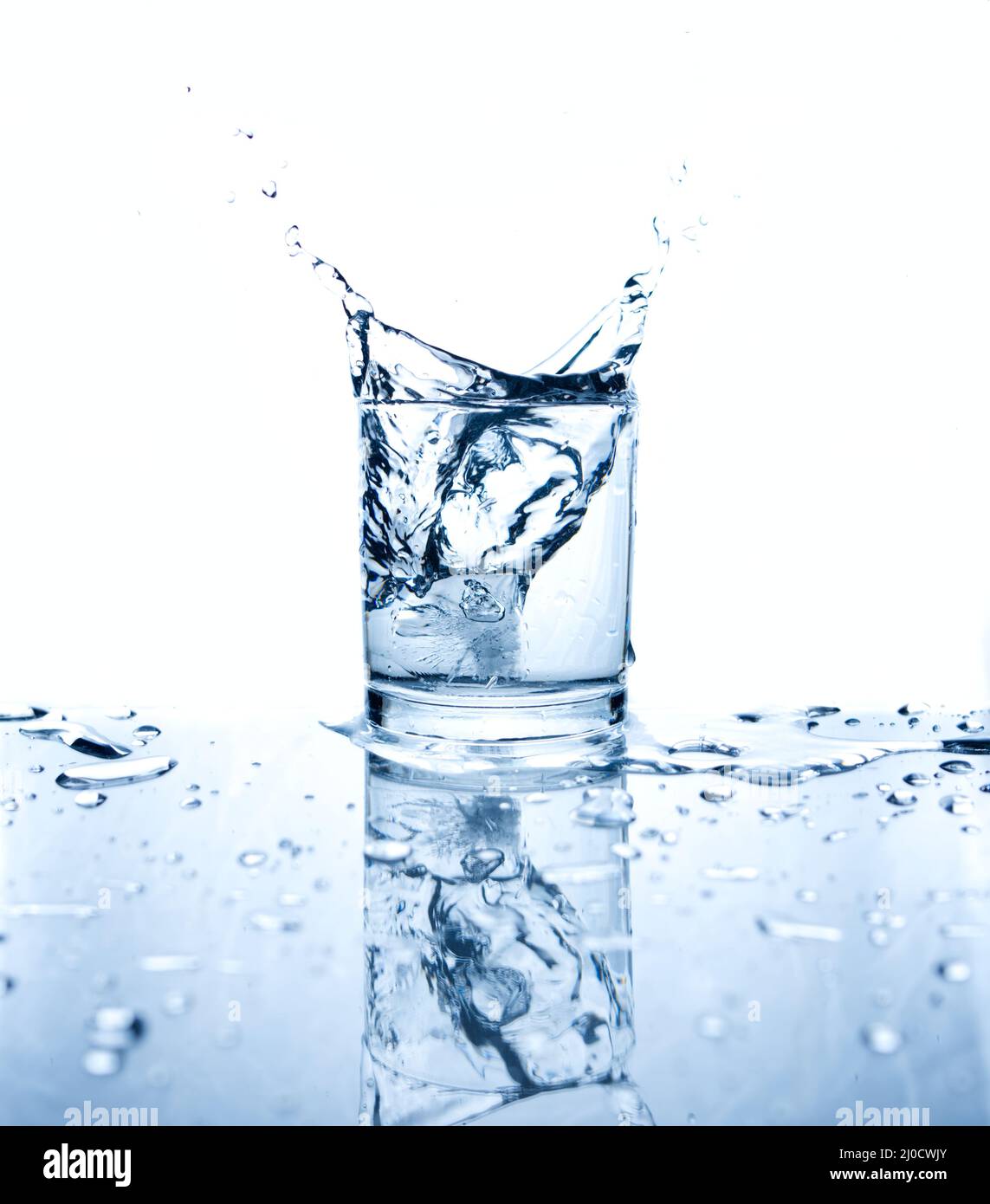Trinkwasser mit Eis in Glas auf weißem Hintergrund mit Reflexen gespritzt. Stockfoto