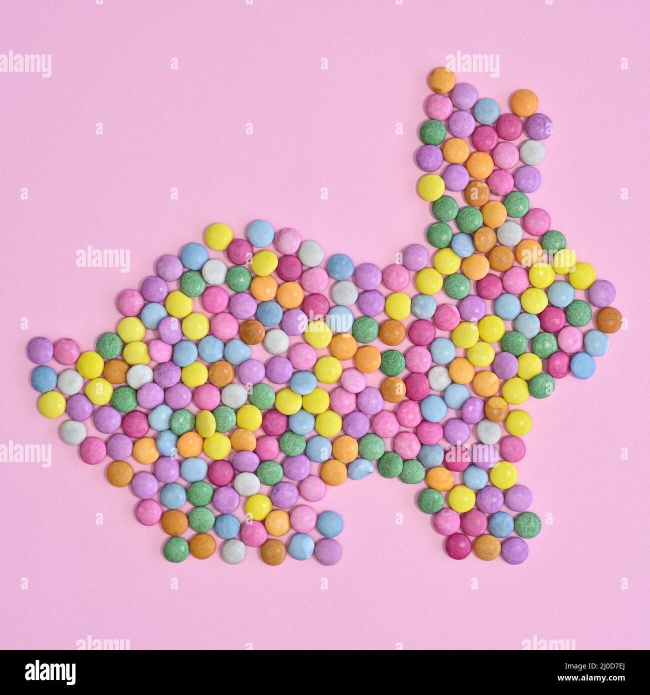Kreativer Kaninchenhase mit farbenfrohen Bonbons auf pastellrosa Hintergrund. Flaches Osterkonzept Stockfoto