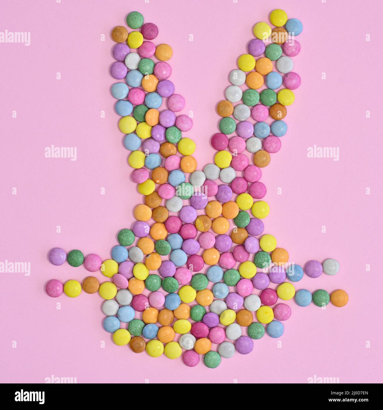 Kreativer Hasenkopf mit farbenfrohen Bonbons auf pastellrosa Hintergrund. Flaches Osterkonzept Stockfoto
