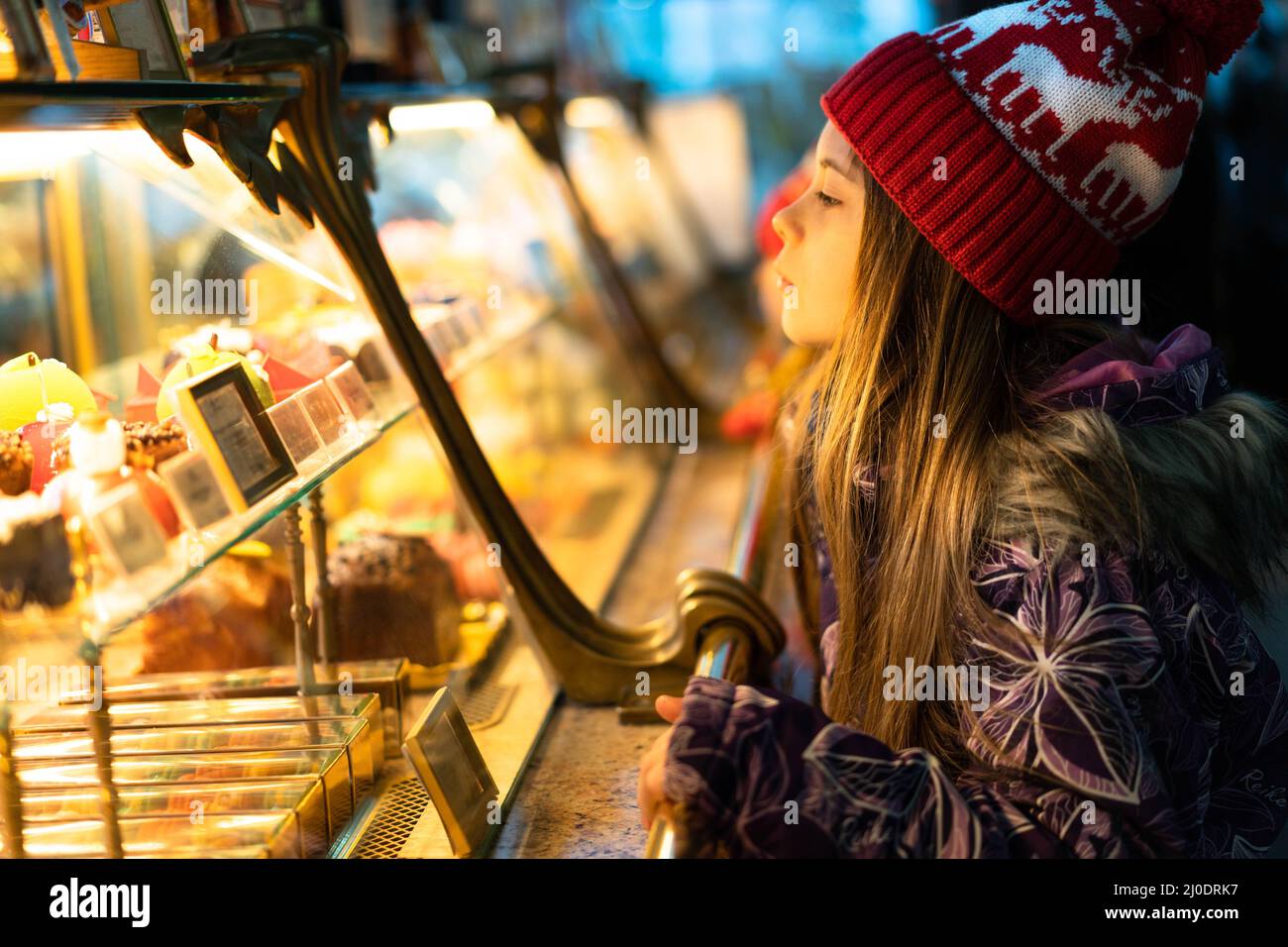 Ein Kind in Winterkleidung und einem weihnachtlichen roten Hut wählt Süßigkeiten in einem Schaufenster aus, um sie zu kaufen. Das Konzept der Neujahrsferien, Rabatte, Shopping. Stockfoto