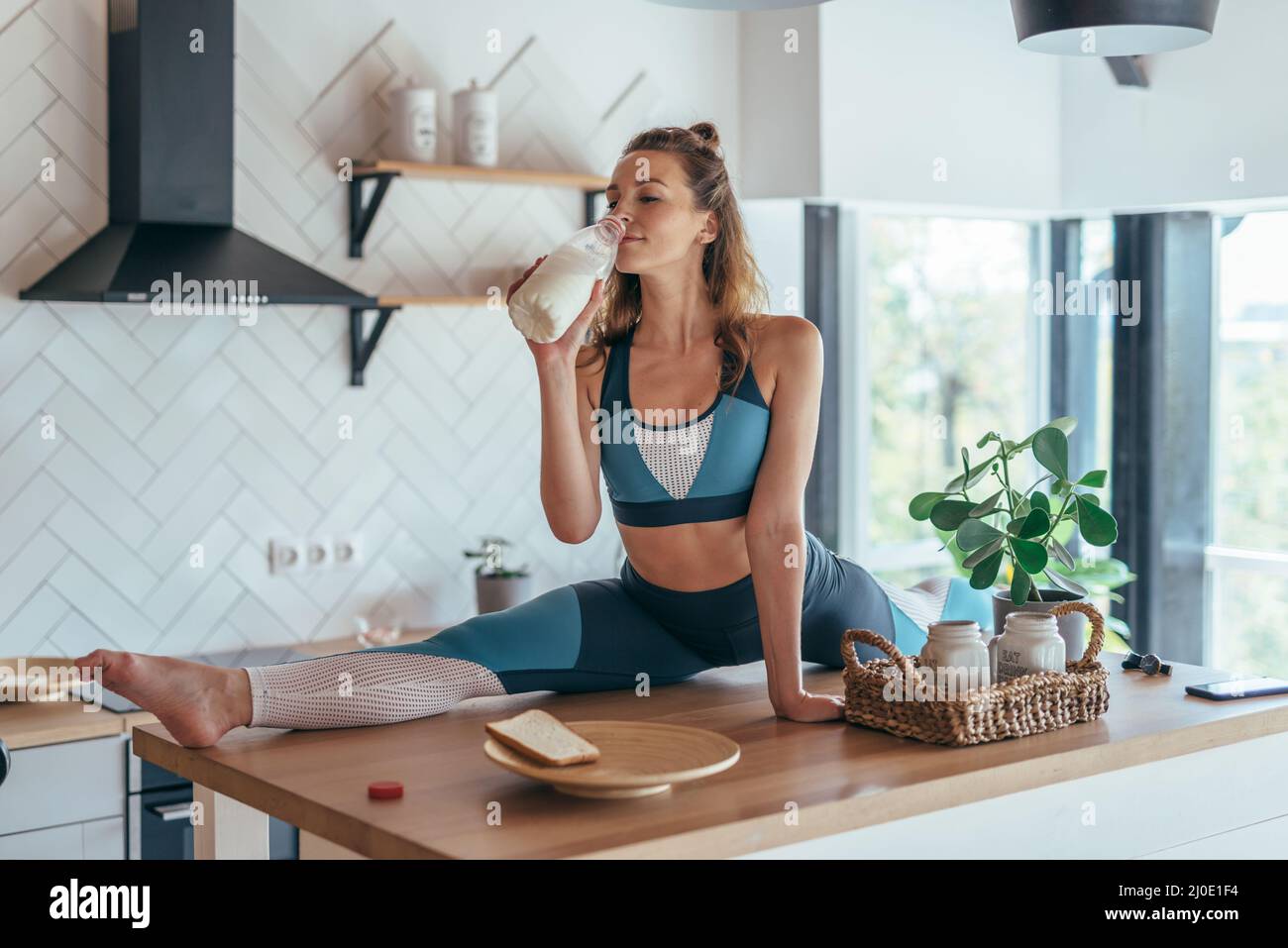 Fit Frau beim Frühstück in geteilter Position auf dem Küchentisch Stockfoto