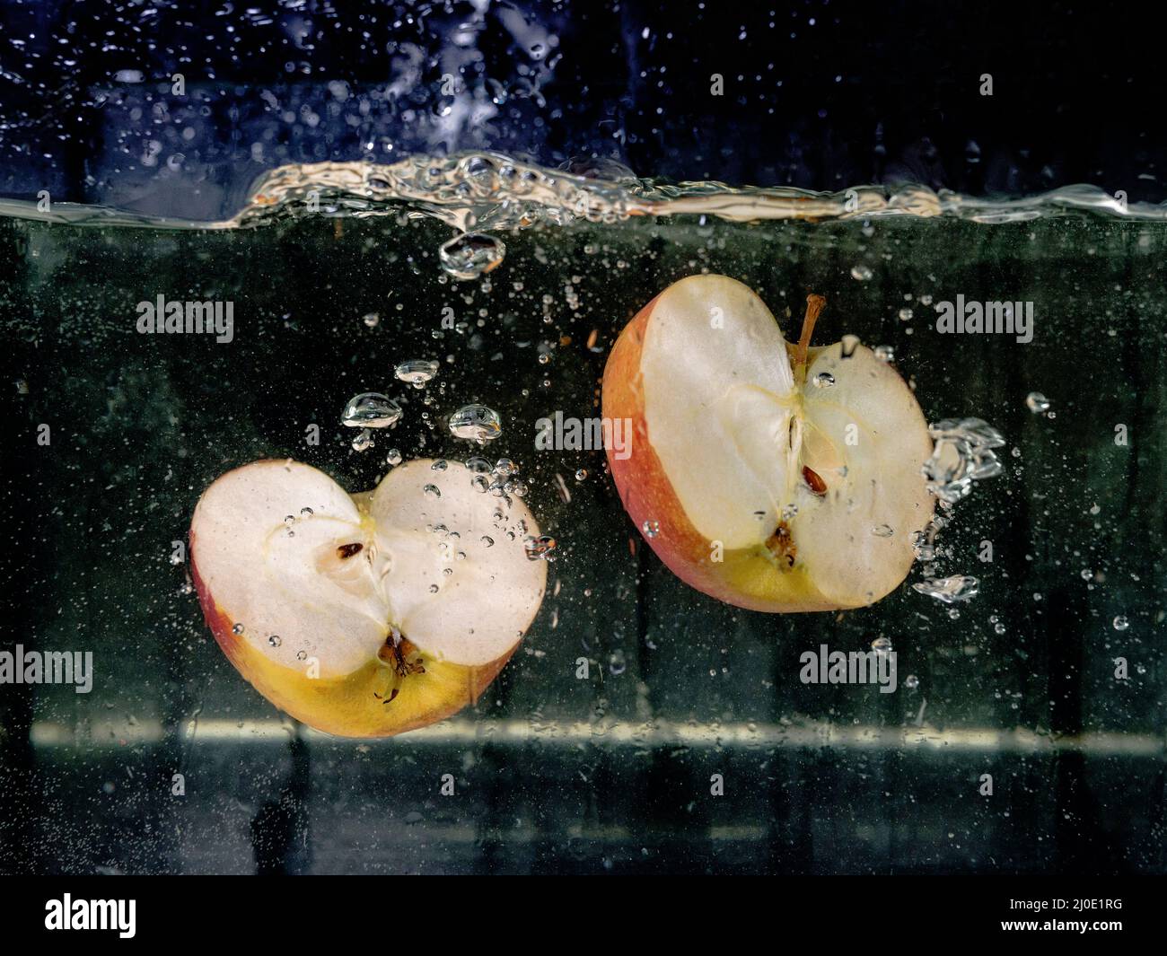 Auf dunklem Grund fallen in Scheiben geschnittene Äpfel ins Wasser. Unterwasseransicht. Kochen, vegetarisch, Kochen zu Hause Konzept Stockfoto