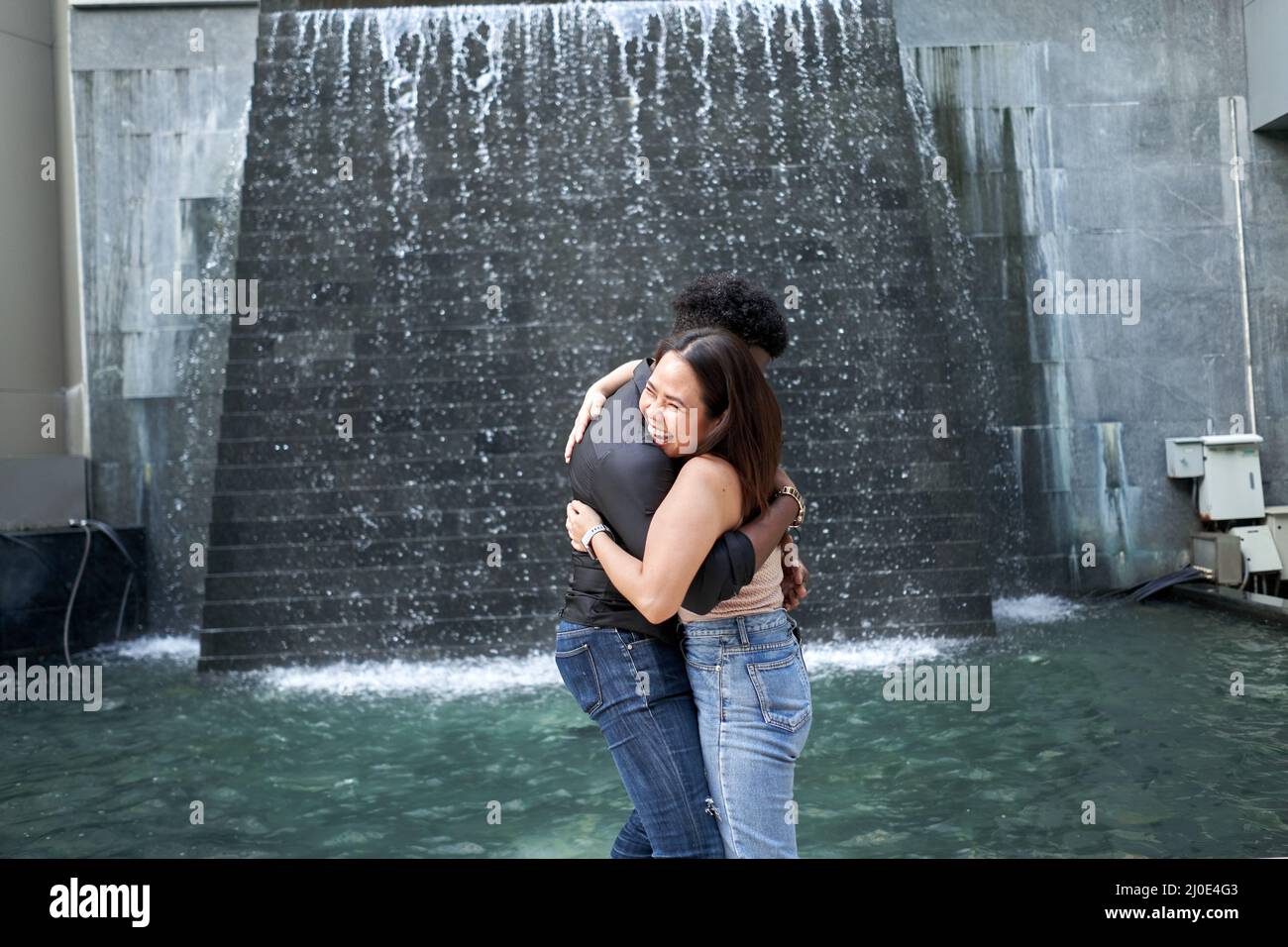 Multiethnische Freunde umarmen sich neben einem künstlichen Wasserfall in einem modernen Einkaufszentrum Stockfoto