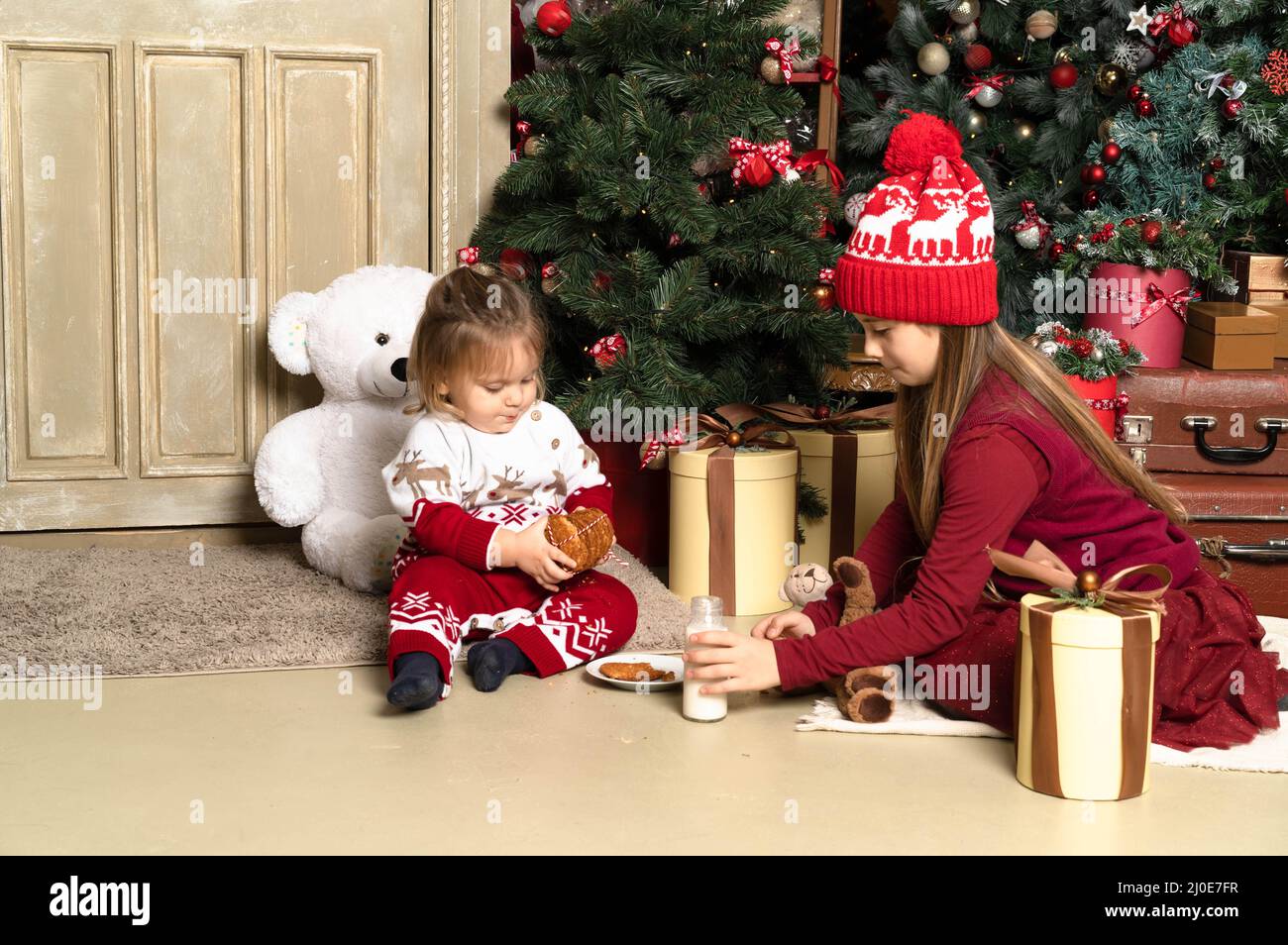 Schwester und Bruder Baby in roten Weihnachtskleidung und Winterpullover und öffnen Neujahrsgeschenke .Horizontales Foto für weihnachten, Vatertag, Weihnachten. Stockfoto