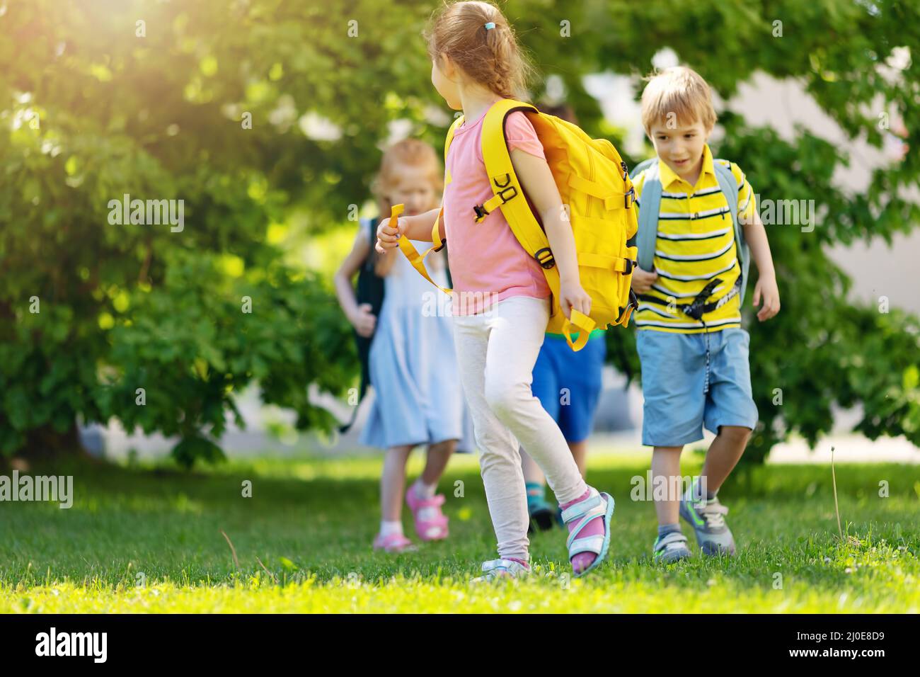 Nette Kinder mit Rucksäcken, die im Park in der Nähe der Schule spazieren gehen Stockfoto