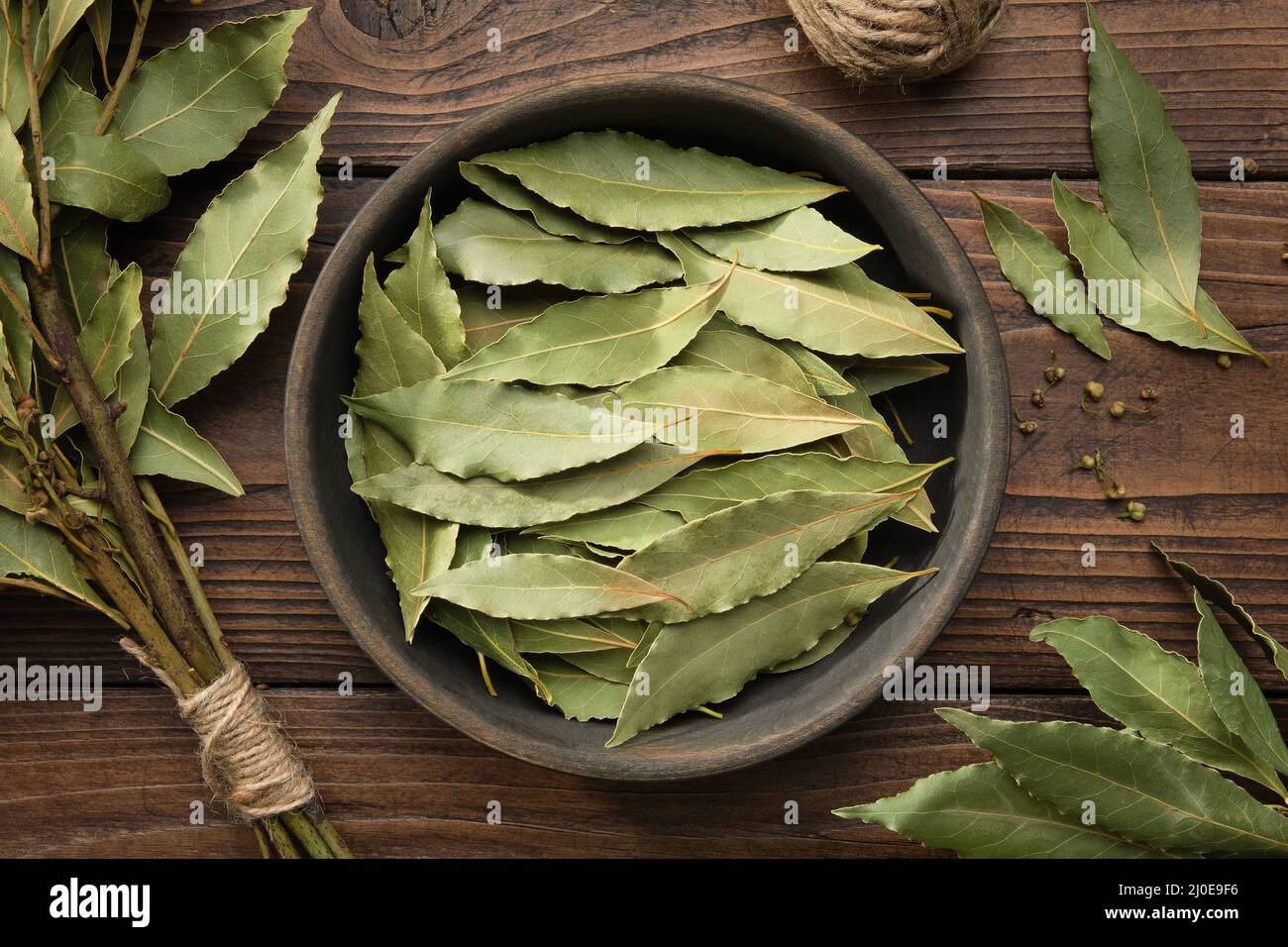 Schüssel mit getrockneten Lorbeerblättern. Zweig der grünen Lorbeerblätter auf Holztisch, Draufsicht. Stockfoto