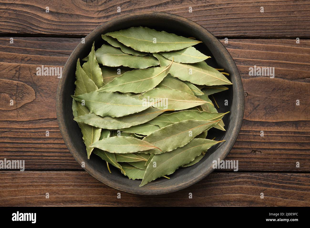 Holzschale aus getrockneten Lorbeerblättern. Grüne Lorbeerblätter auf Holzbrett, Draufsicht. Stockfoto