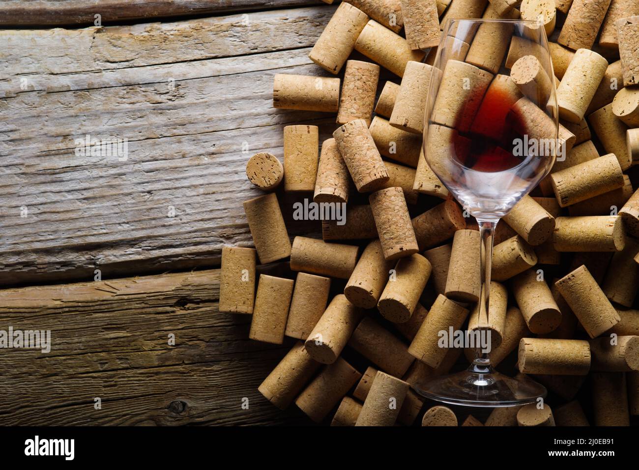 Viele Weinkorken und ein Glas Rotwein auf einem hölzernen Hintergrund. Auf dem Foto befinden sich keine Personen. Restaurant, Hotel, Weinkeller, Weinprobe, gewinnen Stockfoto