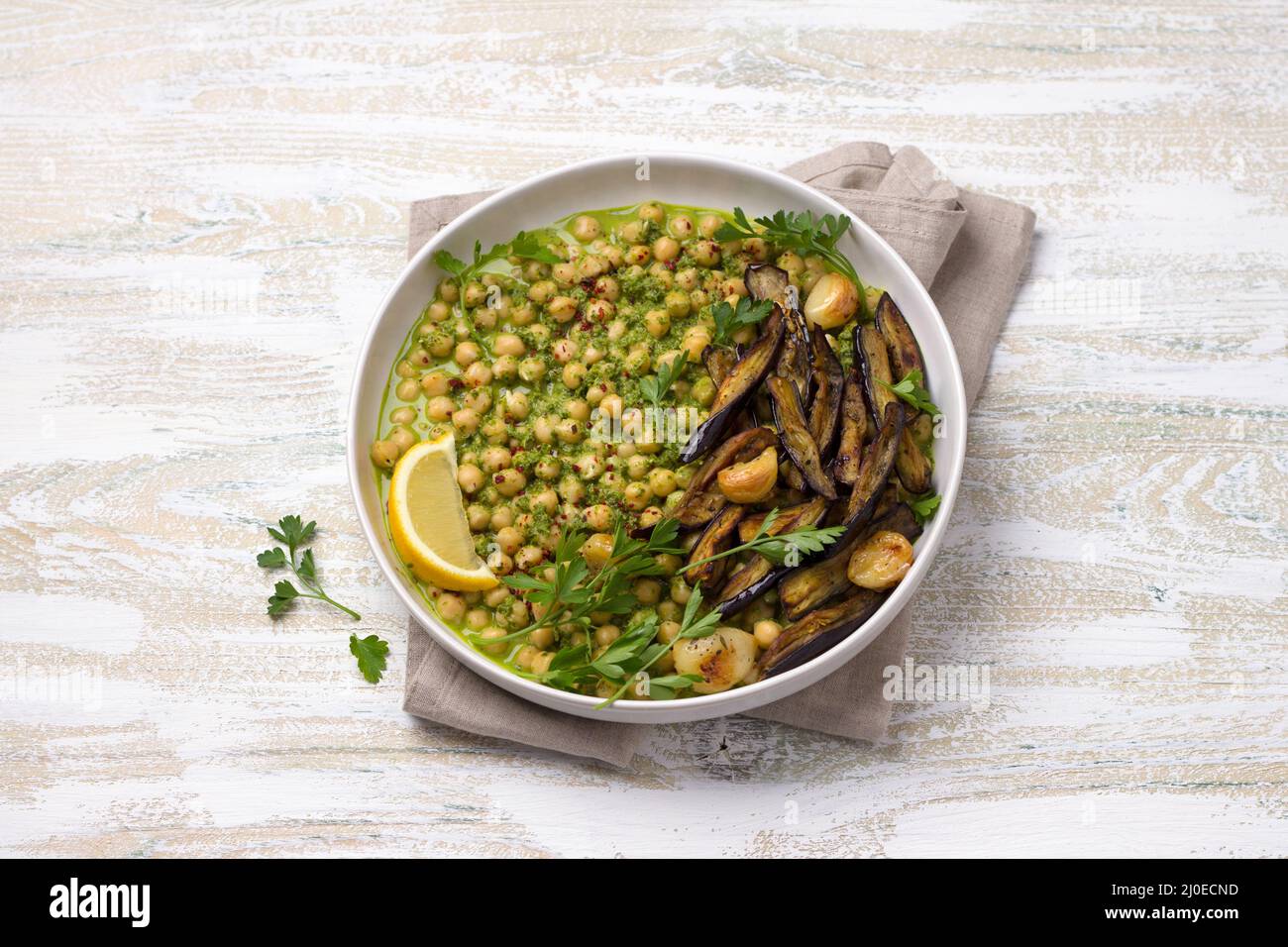 Geschmorte Kichererbsen in grüner Sauce mit gebackener Aubergine, Petersilie und Zitrone auf weißem Holzhintergrund, rustikaler Stil, Draufsicht. Leckeres gesundes Zuhause Stockfoto