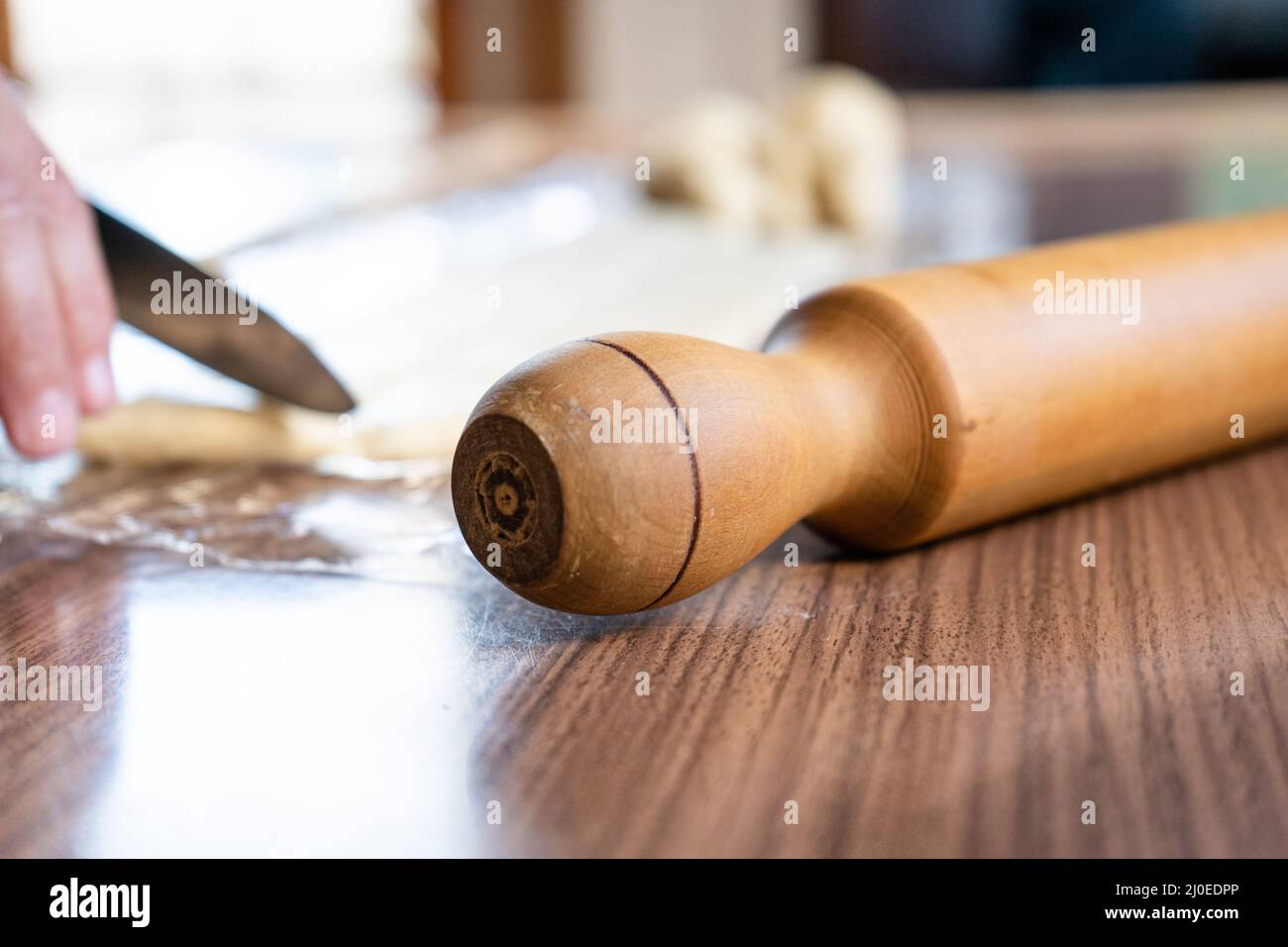 Nahaufnahme eines Nudelnadels auf einem Holztisch mit einer Hand und einem Messer dahinter Stockfoto