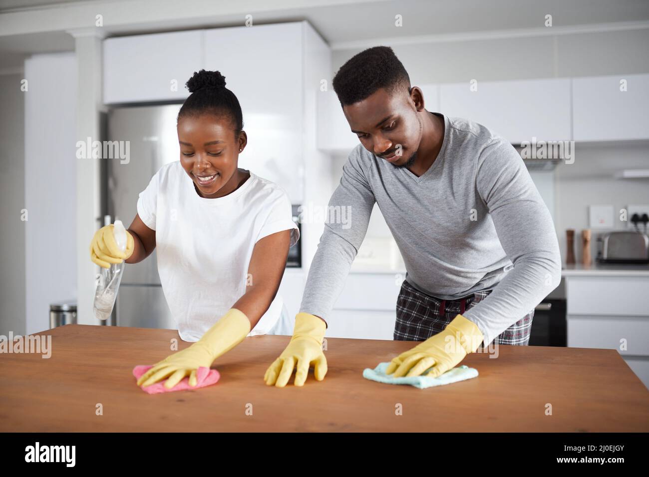 Ein wenig Ellenbogenfett sorgt für einen Glanz nach Hause. Aufnahme eines jungen Paares, das zu Hause die Küchentheke putzt. Stockfoto