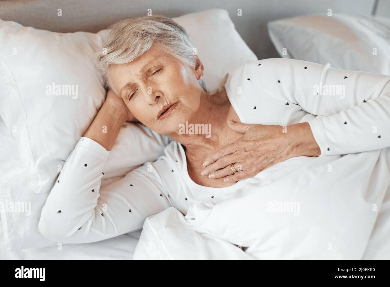 Es kann jedem passieren. Aufnahme einer älteren Frau mit Brustschmerzen im Bett in einem Pflegeheim. Stockfoto