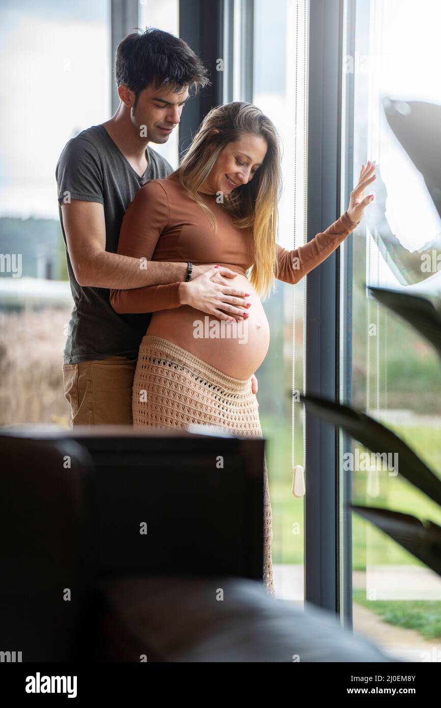 Ein junger Mann umarmte ihre Schwangere am Fenster Stockfoto