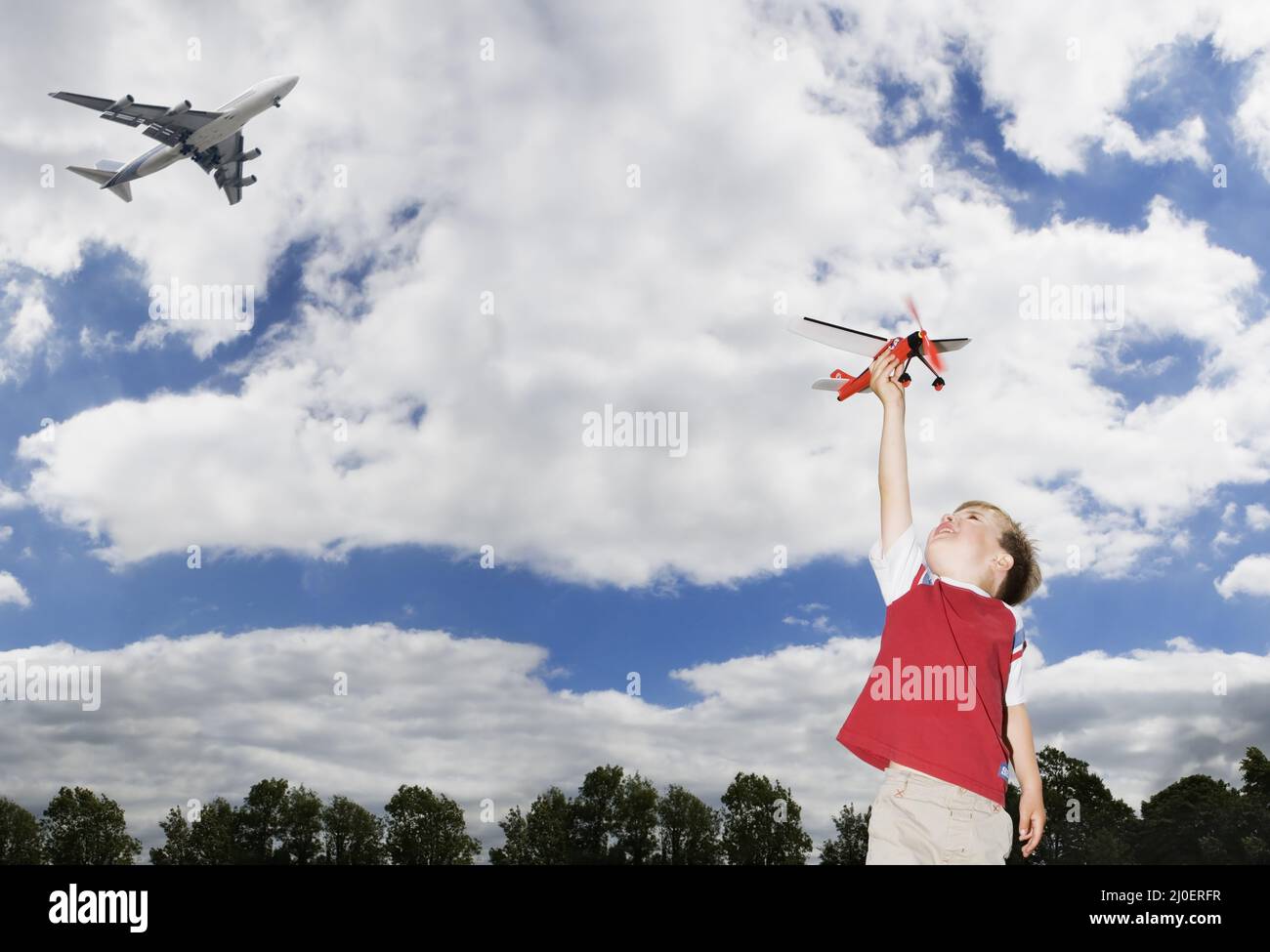 Junger kaukasischer Junge, der mit einem Spielzeugflugzeug spielt, während ein Passagierflugzeug über Themen der Zukunft fliegt Stockfoto