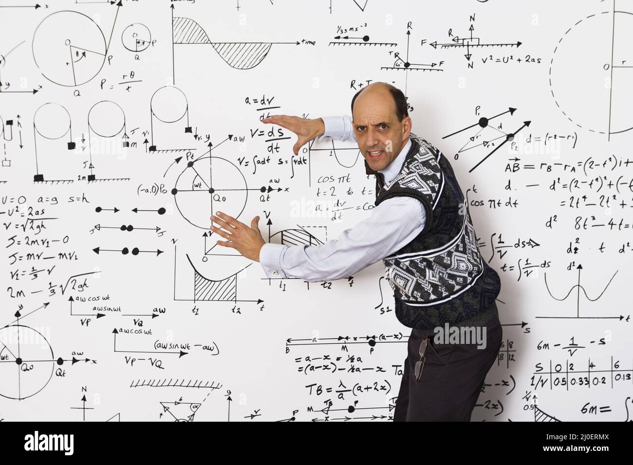 Kaukasischer Mathematiker mittleren Alters, der mathematische Gleichungen an einer weißen Wand erklärt Stockfoto