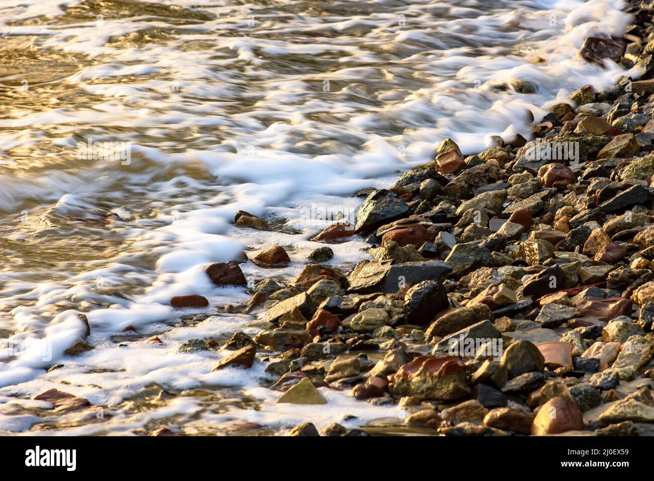 Kleine Steine am Ufer mit dem Schaum Stockfoto