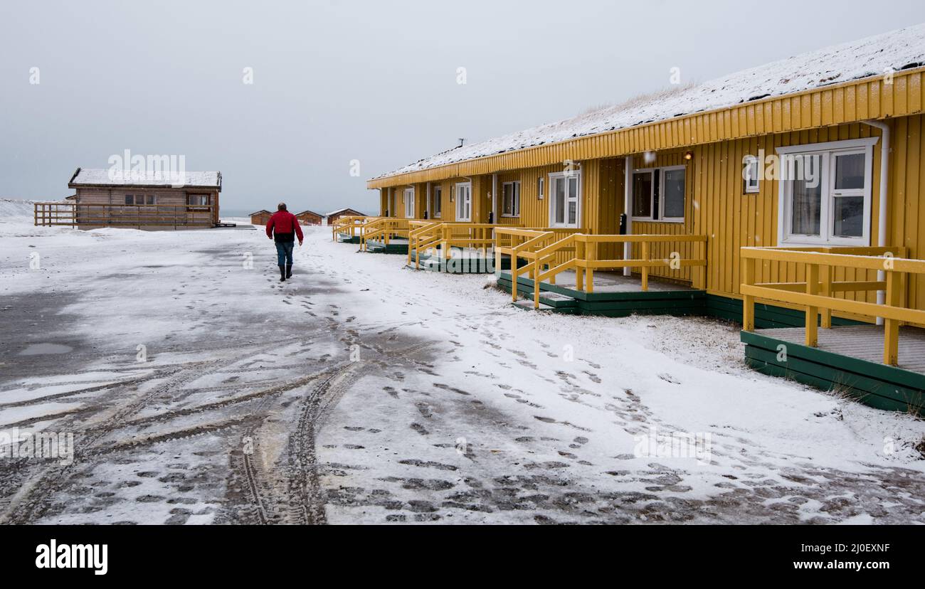 Mann, der auf einer verschneiten Straße zum gelben Winterhaus in Island geht Stockfoto