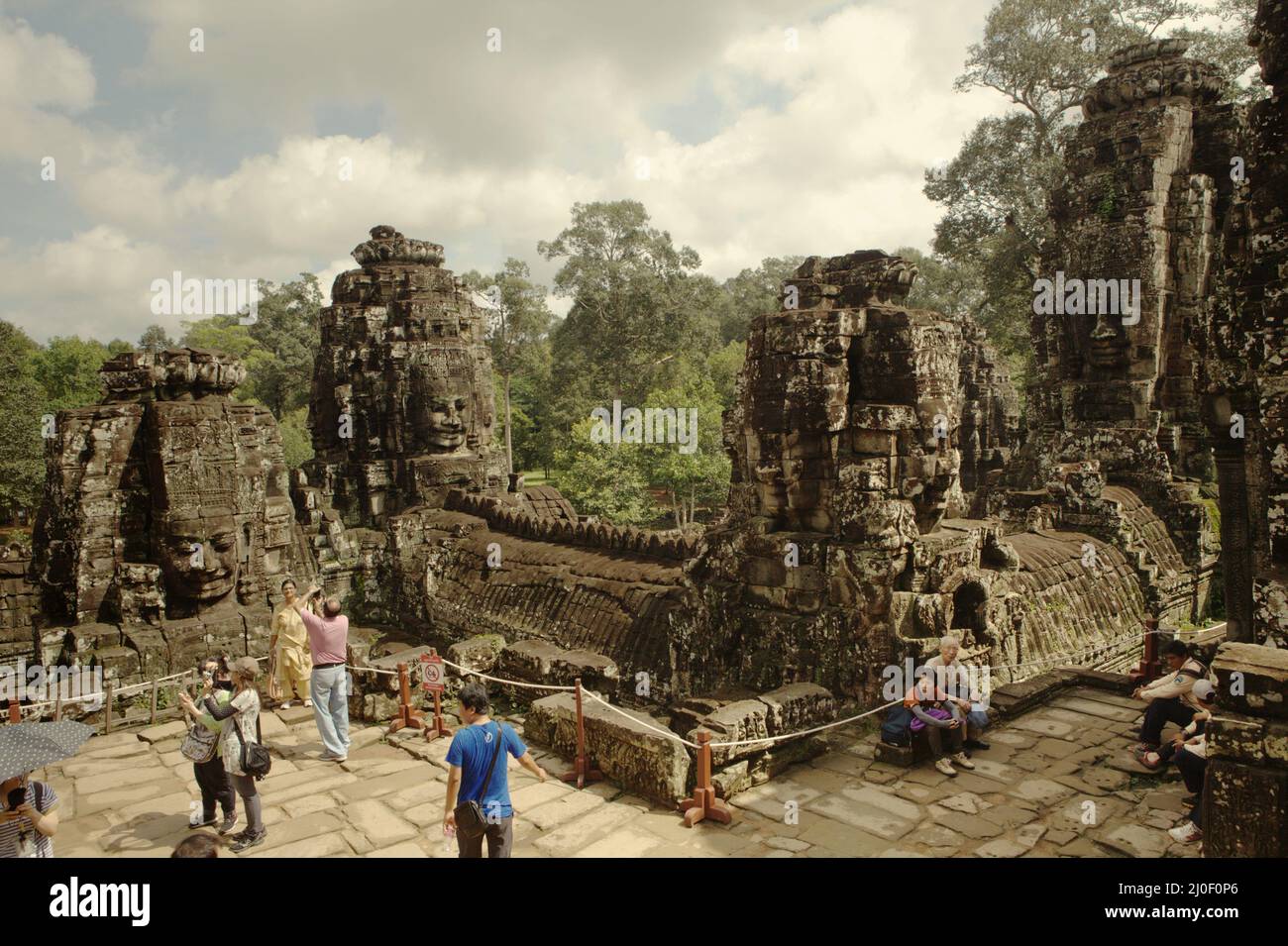 Besucher, die sich unter den riesigen Steintürmen, die mit lächelnden Gesichtern verziert sind, Zeit für Besichtigungen am Prasat Bayon (Bayon Tempel) in Angkor Thom, dem Zentrum der alten angkorianischen Stadt, die die größte und bevölkerungsreichste Stadt der Welt war, in der bis zu 900.000 Menschen lebten, Bis Kriege und Klimakatastrophen in den Jahren 14. und 15 die Jahrhunderte dazu gezwungen hatten, sie aufzugeben. Credits: PACIFIC Imagica/Alamy Stockfoto
