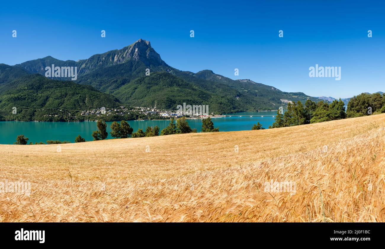 Blick auf den Serre-Poncon-See mit dem Dorf Savines-le-Lac und dem Grand Morgon Peak mit Weizenfeldern. Hautes-Alpes (Alpen). Frankreich Stockfoto