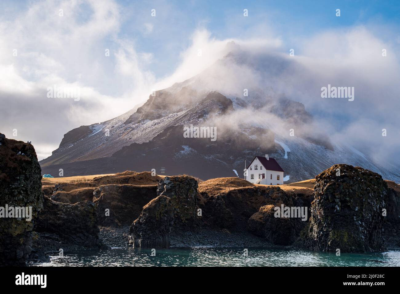 Isländische Landschaft, schneebedeckter Vulkan und einsames Haus im Winter in Arnarstapi Dorf. Stockfoto