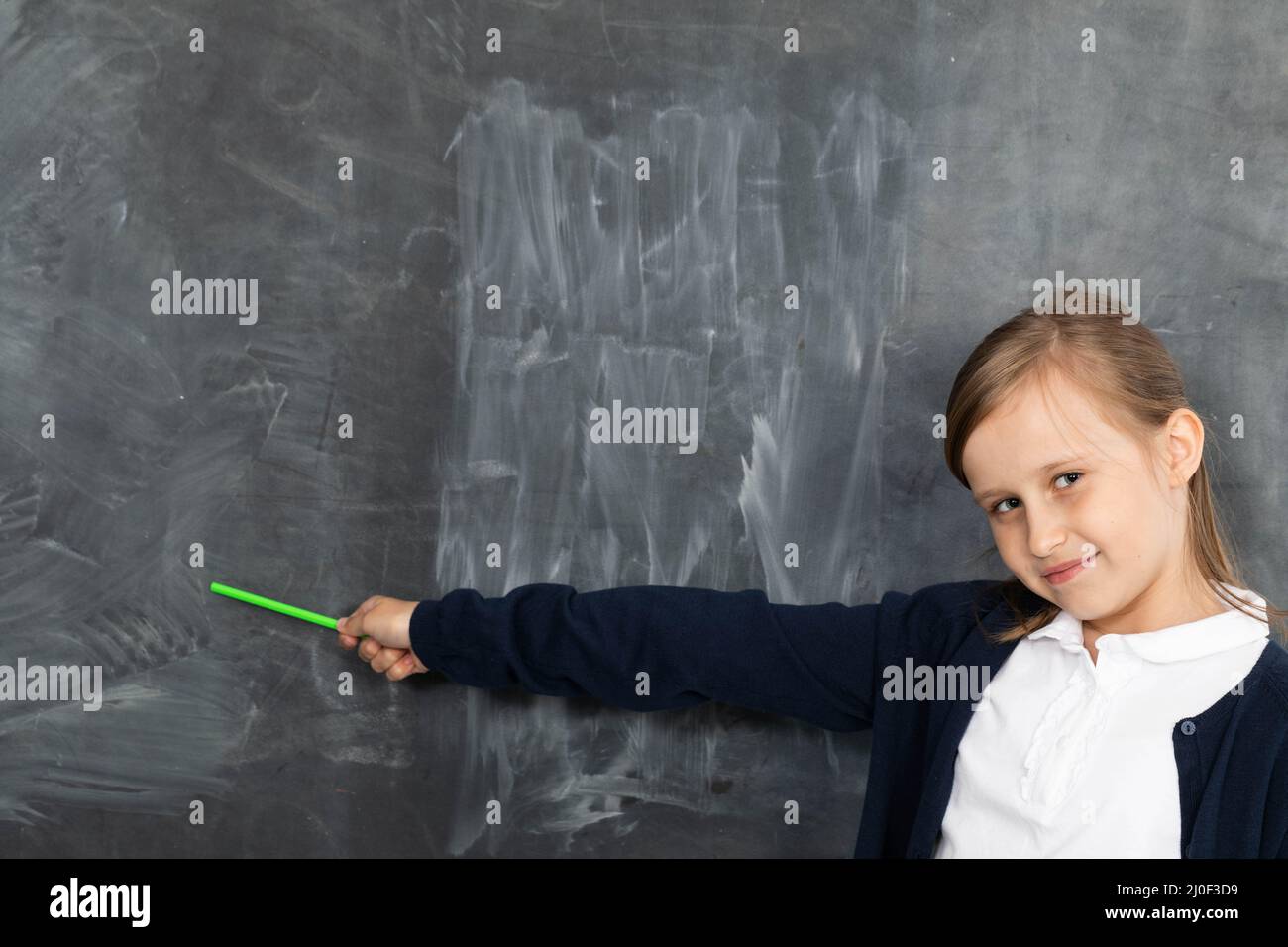 Schulmädchen zeigt auf einem leeren Schulbrett. Er steht im Klassenzimmer an der Tafel. Jüngeres Mädchen. Stockfoto