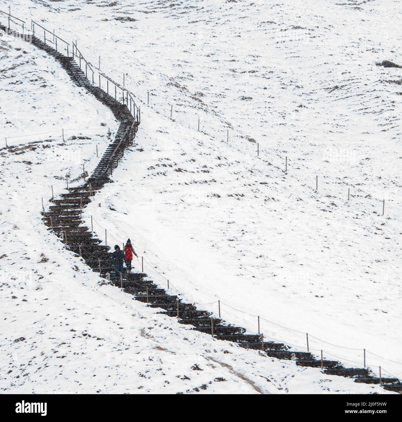 Menschen, die auf einem verschneiten Naturlehrpfad am Skogafoss Wasserfall in Island wandern Stockfoto