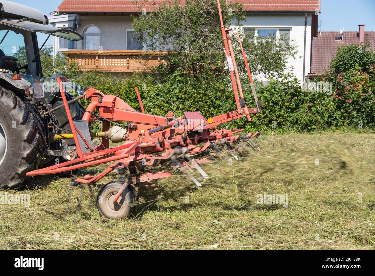 Gemähtes Gras wird von einem Landwirt mit einem Rechen für die Heuschrecke gedreht - Zettwender Stockfoto