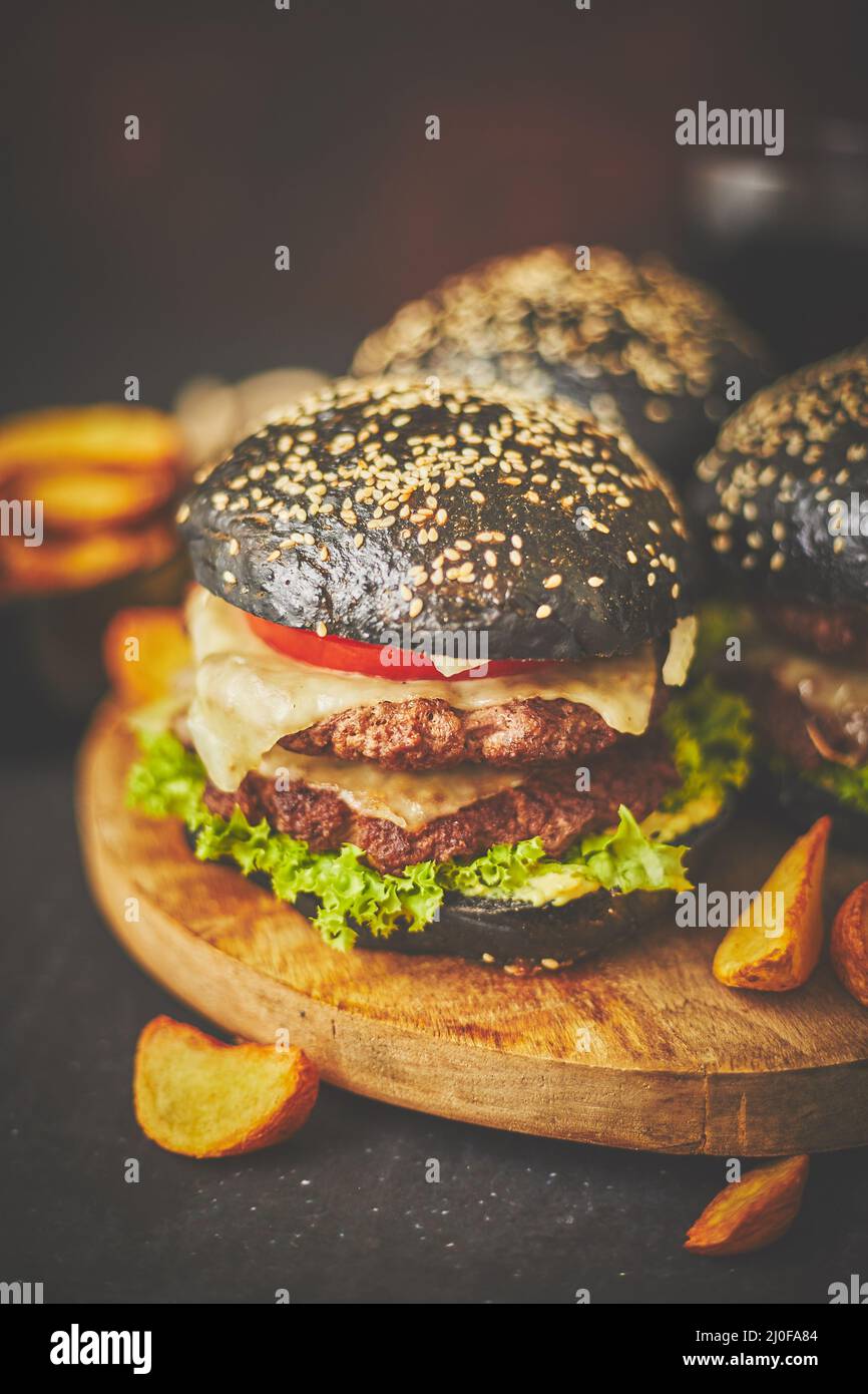 Schwarze doppelte Burger mit Käse. Cheeseburger aus Japan mit schwarzem Brötchen auf dunklem Hintergrund Stockfoto