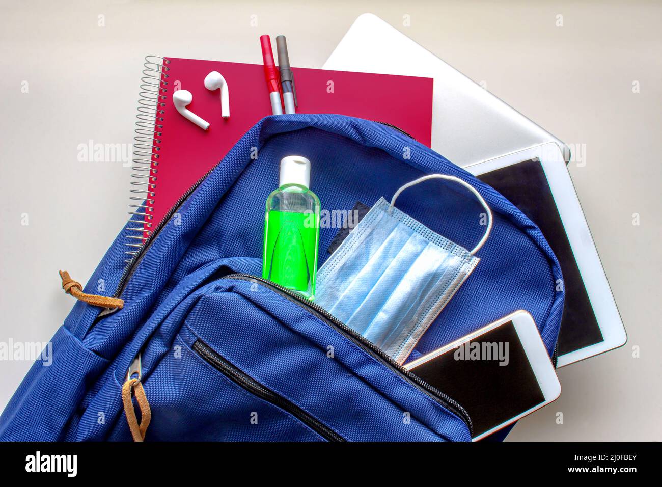 Eine blaue Schultasche mit Desinfektionsmittel und einer Gesichtsmaske, Stiften, Ohrhörern, Tablet, Computer und einem Smartphone. Zurück zur Schule duri Stockfoto