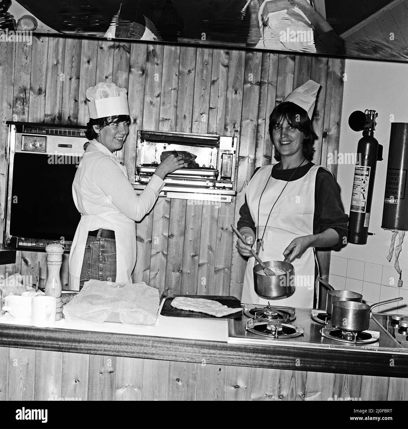 Prudence Leith (auch bekannt als Prue Leith) links im weißen Hemd unter ihrer weißen Schürze, zusammen mit Caroline Waldergrave rechts mit ihrem schwarzen Hemd unter ihrer weißen Schürze. Prue und Caroline sind Autoren eines neuen Kochbuches - Leith's Cookery Course Book 1 - und werden gesehen, wie sie sich heute Abend auf die Ankunft eines ihrer abendlichen Kochkurse vorbereiten. Bild aufgenommen am 24.. Oktober 1979 Stockfoto
