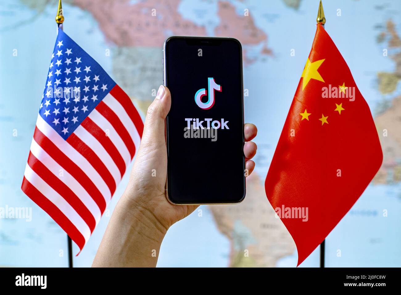 Calgary, Alberta, Kanada. September 8, 2020. Eine Person, die ein iPhone mit dem Bildschirm der TikTok App neben einer Flagge der USA und Chinas auf einem hält Stockfoto
