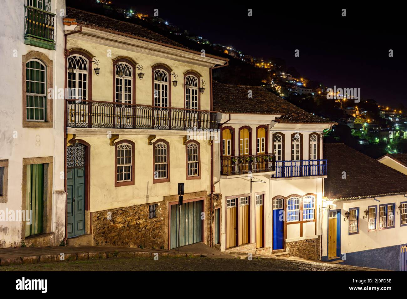 Fassaden von Häusern in Kolonialarchitektur auf einer alten Kopfsteinpflasterstraße, die nachts beleuchtet wird Stockfoto