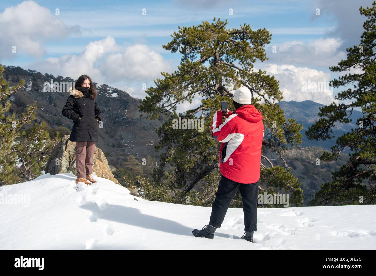 Zwei junge glückliche Teenager, die mit einem Mobiltelefon auf einem verschneiten Berg Fotos machen. Stockfoto