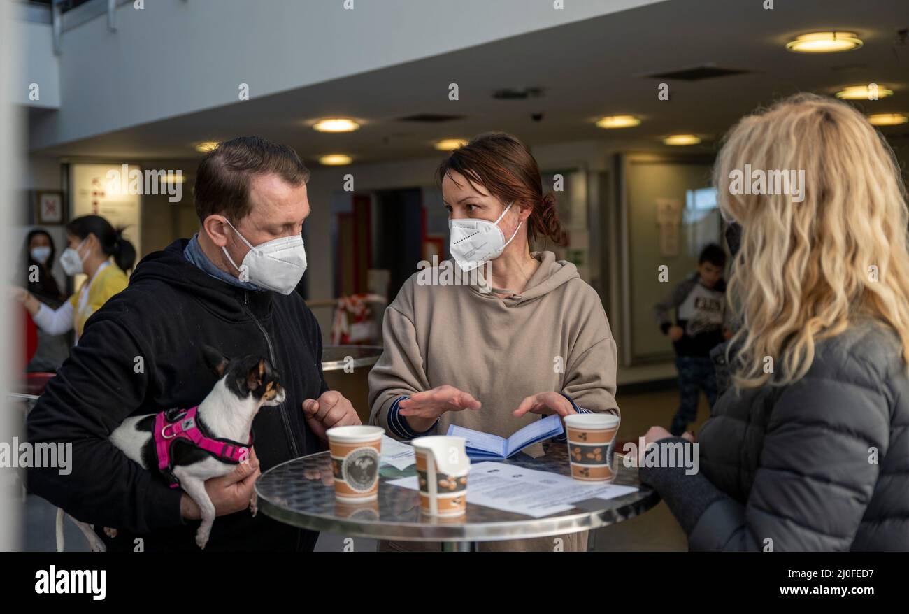 Berlin, Deutschland. 18. März 2022. Tierärztin Karin Elisabeth Lason (M) spricht im Hauptterminal des ehemaligen Flughafens Berlin-Tegel mit einem Paar aus der Ukraine über die notwendigen Impfungen für ihren Hund Tessa. In den Räumen des alten Hauptterminals des Flughafens TXL wurde in den letzten Wochen ein Ankunftszentrum für ukrainische Kriegsflüchtlinge errichtet. (To dpa 'Etagenbetten und Kinderbilder - neues Leben am alten Flughafen Tegel') Quelle: Monika Skolimowska/dpa-Zentralbild/dpa/Alamy Live News Stockfoto