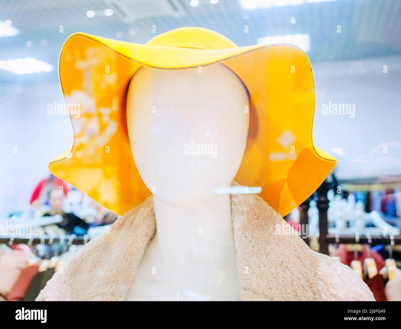 Abstrakte Schaufensterpuppe Kopf in gelben Hut auf verschwommenem Shop Hintergrund Stockfoto