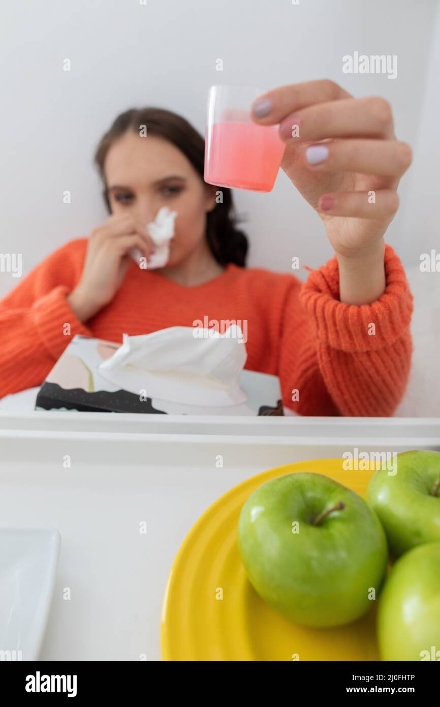 Ein kranker Teenager trinkt flüssige Medizin, die in eine kleine Tasse gegossen wird. Stockfoto