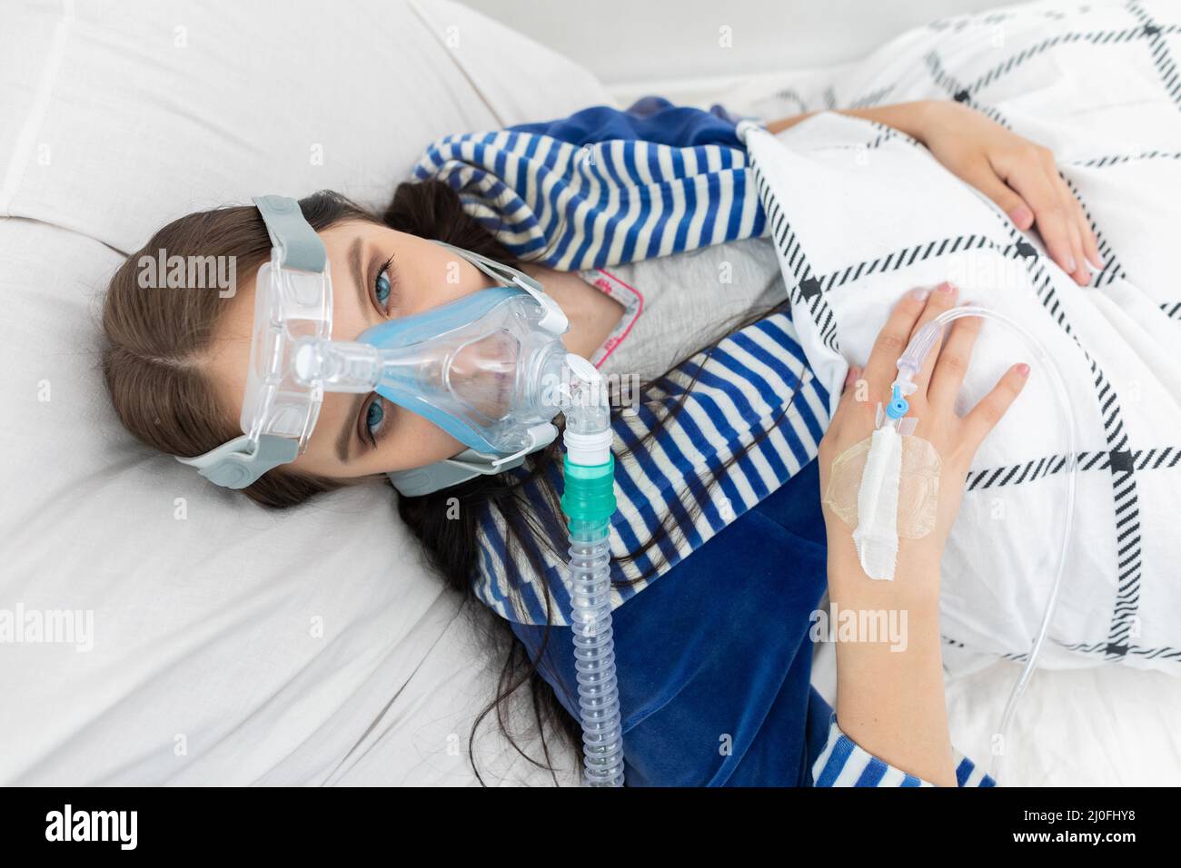 Schwerkranke Jugendliche, die an ein Atemschutzgerät angeschlossen sind, um die Atmung zu unterstützen. COVID-19-Infektion. Stockfoto
