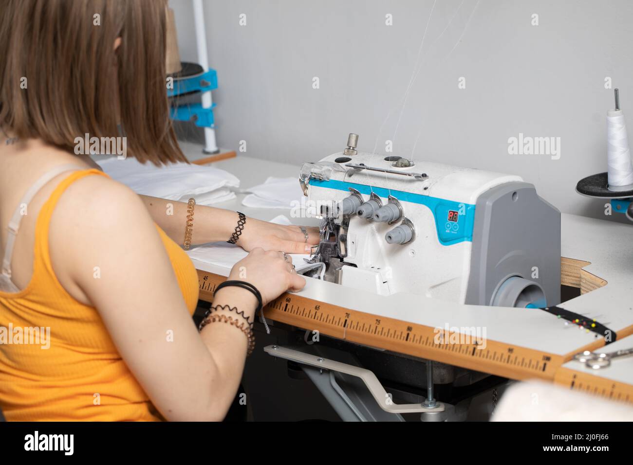 Ein Teenager-Schulmädchen lernt, während einer Pandemie Schutzmasken auf einen Overlock zu nähen. Stockfoto