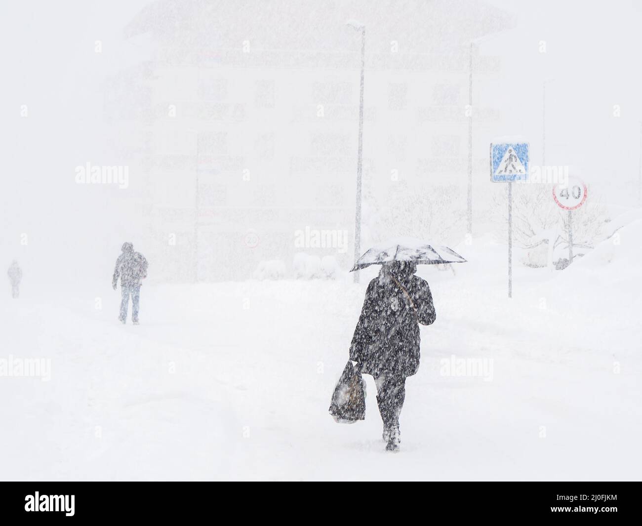 Eine Frau mit einem Sonnenschirm läuft auf einer schneebedeckten Straße Anderen Menschen bei starkem Schneefall folgen Stockfoto